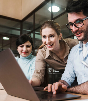 Three individuals gathered around a laptop, intently discussing its screen content.