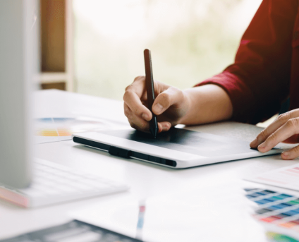 A person working on a computer and taking notes while designing clothing brand logos for fashion brands.